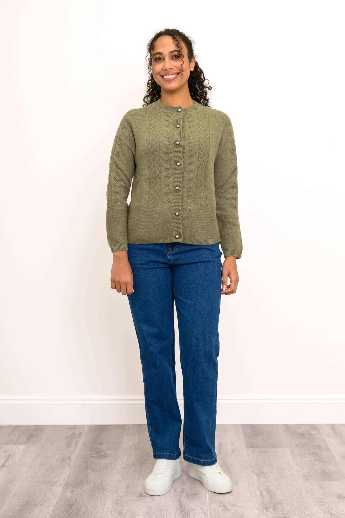 Woman standing and smiling in an olive green cable knit cardigan and blue jeans