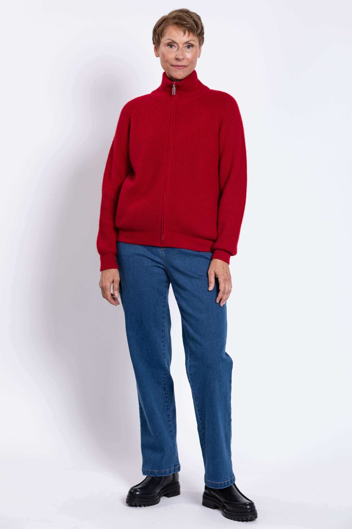 Person posing in red zip-up ribbed cardigan, blue jeans, and black boots