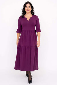 Woman in purple Bernadette midi dress standing and smiling, showing tiered silhouette