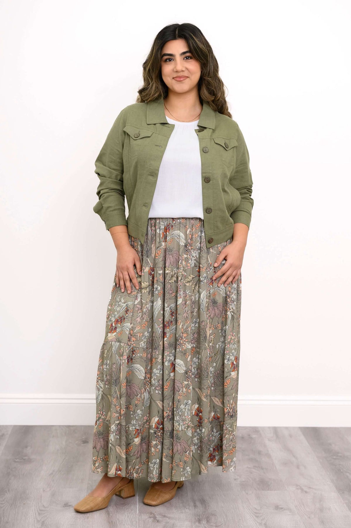 Woman standing in green jean jacket and floral print maxi skirt with tan shoes