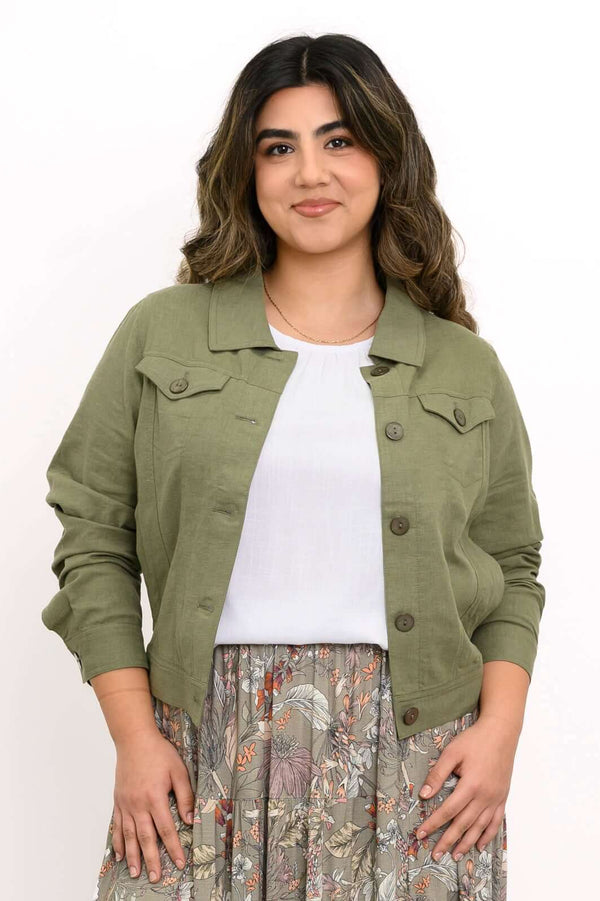 Woman standing in green jean jacket and floral print maxi skirt with tan shoes