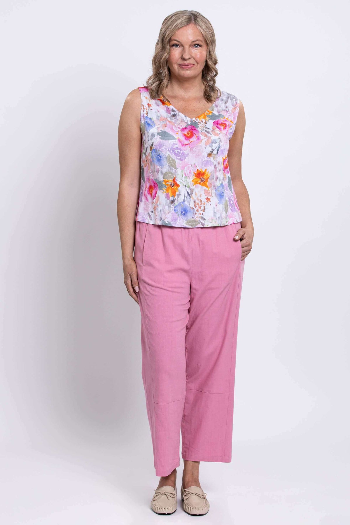 Standing pose of woman wearing floral cropped tank, pink pants, and beige shoes
