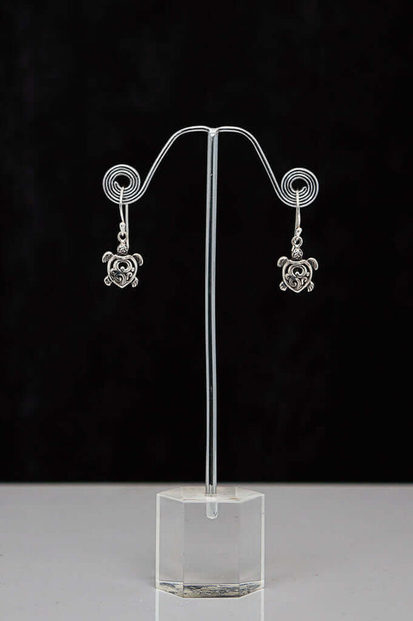 Pair of sterling silver turtle heart earrings displayed on a metal stand with black background