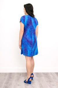 Woman wearing a blue patterned dress and blue sandals on a white background, back view