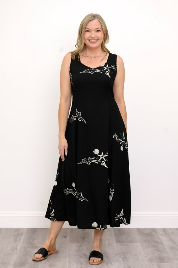 Woman wearing a long black sleeveless dress with white seashells and sandals against a white background, front view