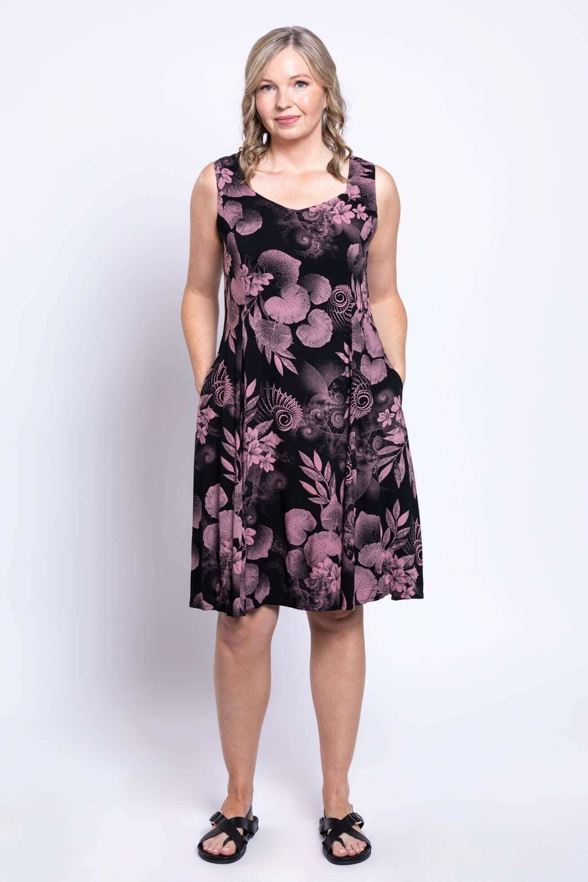 Woman wearing Sweet Sara dress with hands in pockets, pink botanica print