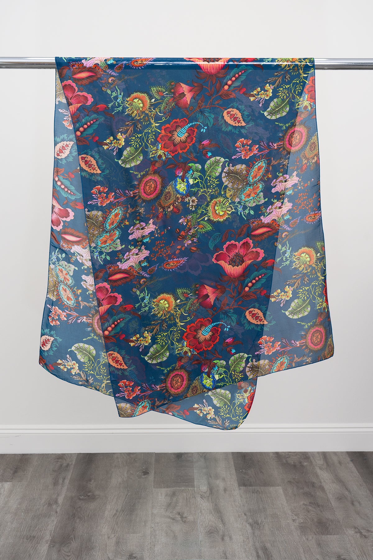 A large teal silk scarf with a multicolour paisley pattern displayed on a metal rod against a white background, front view