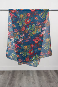 A large teal silk scarf with a multicolour paisley pattern displayed on a metal rod against a white background, front view