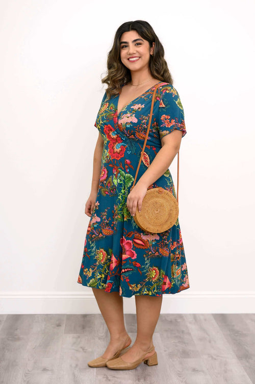 Woman in teal floral bamboo dress, angled to side, holding a round wicker bag