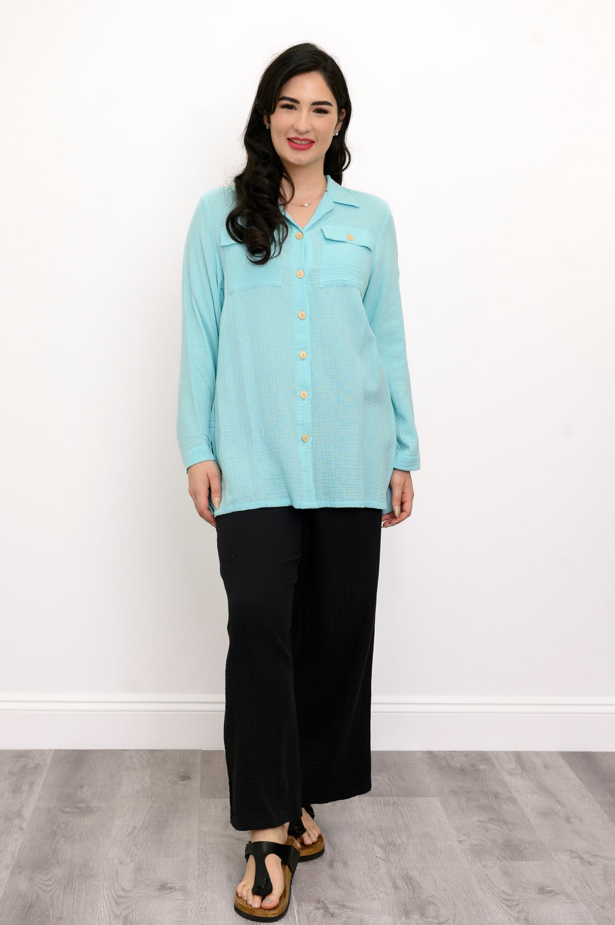 Woman wearing a light blue button-up shirt and black pants against a white background, front view