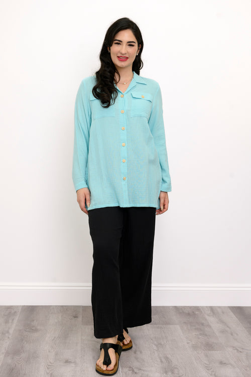 Woman wearing a light blue button-up shirt and black pants against a white background, front view