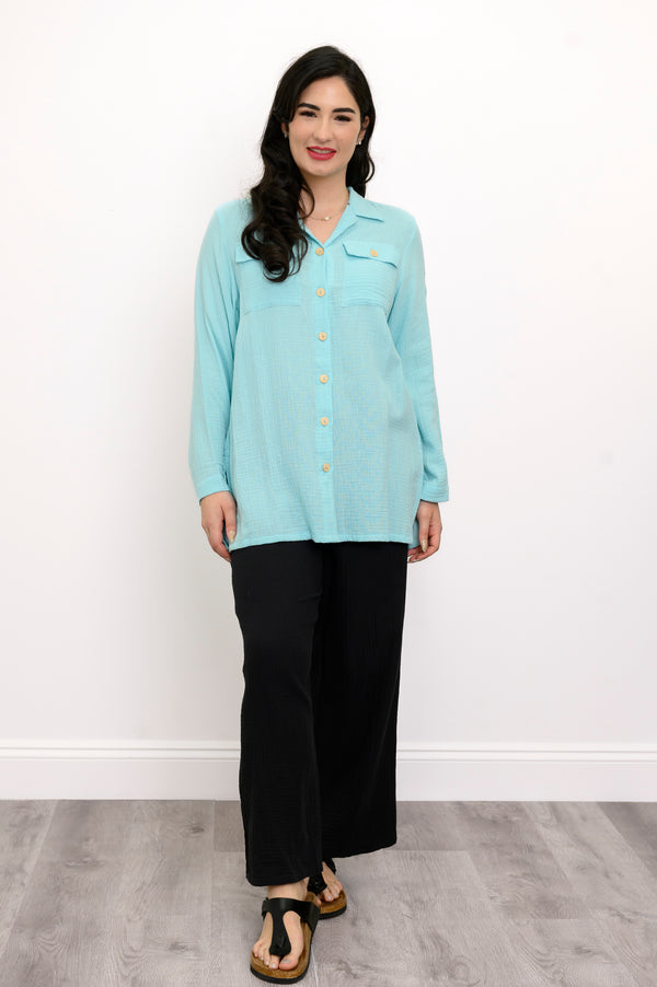 Woman wearing a light blue button-up shirt and black pants against a white background, front view