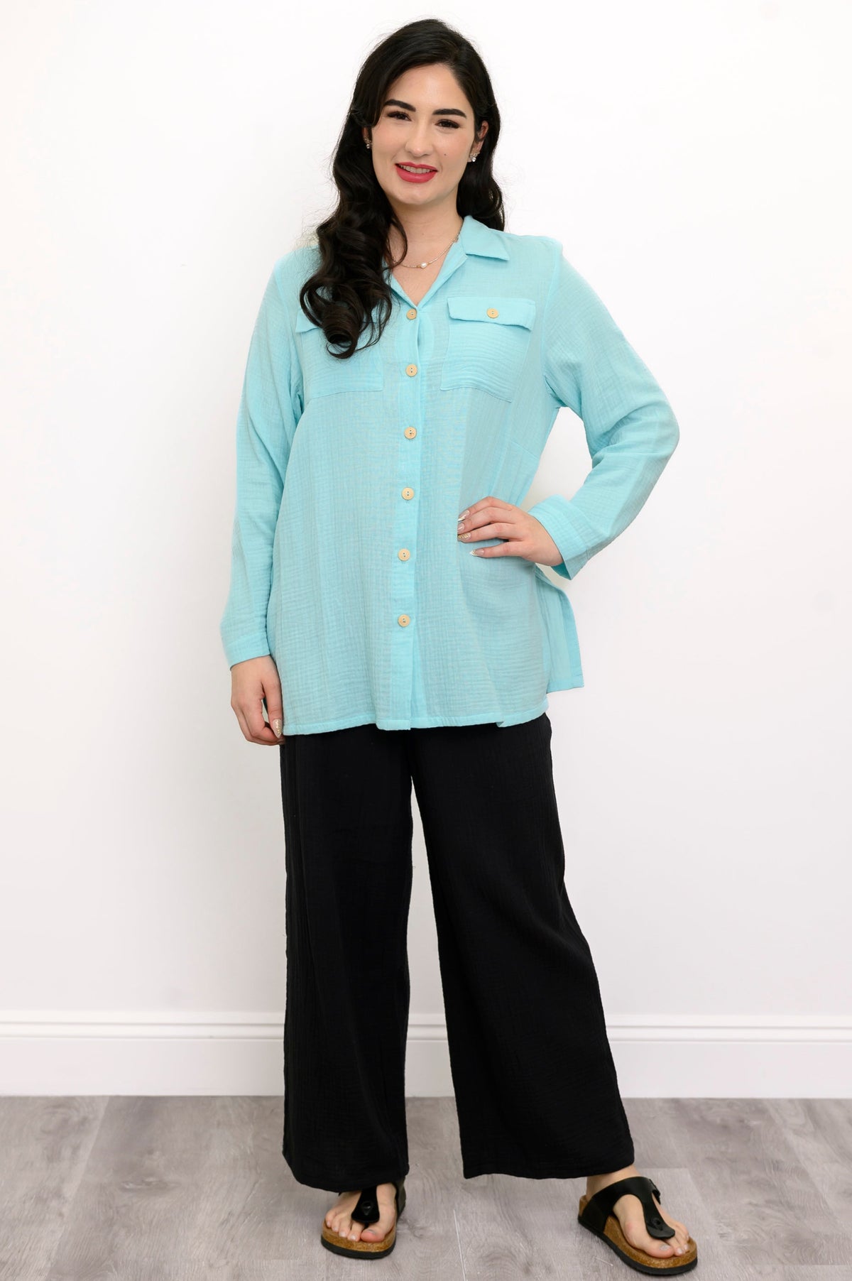 Woman wearing a light blue button-up shirt and black pants against a white background, front view