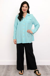 Woman wearing a light blue button-up shirt and black pants against a white background, front view