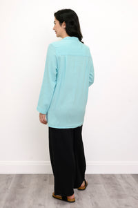 Woman wearing a light blue button-up shirt and black pants against a white background, back view