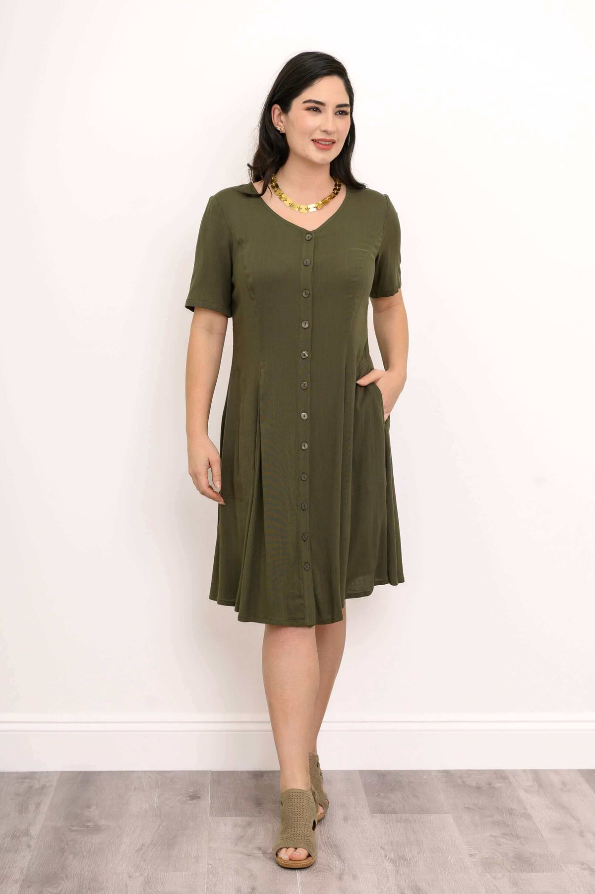 Woman in olive dress styled with gold necklace, button-front and tie-back detail