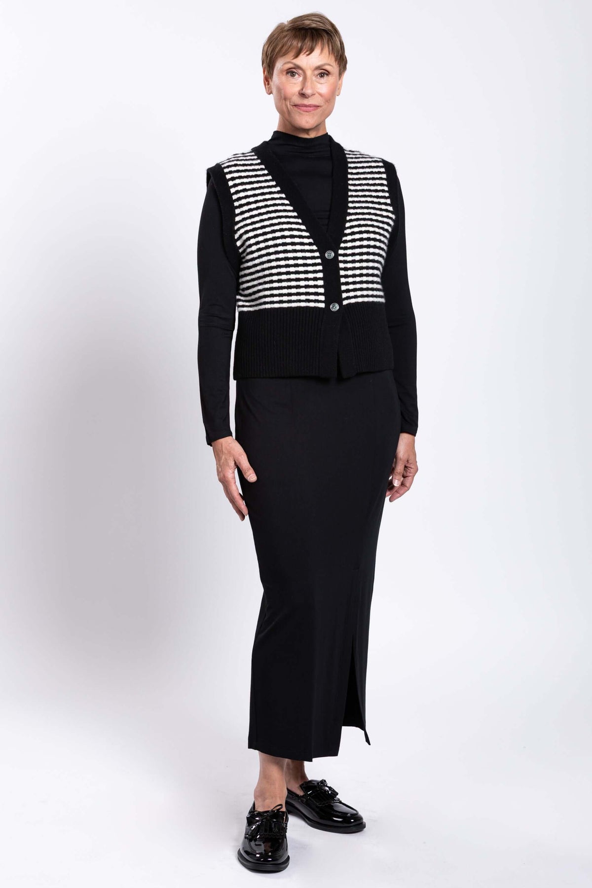 Three-quarter front view of model wearing black and white striped vest and black skirt