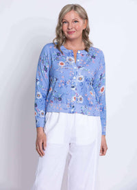 Three-quarter front view of a woman in a blue floral cardigan and white pants