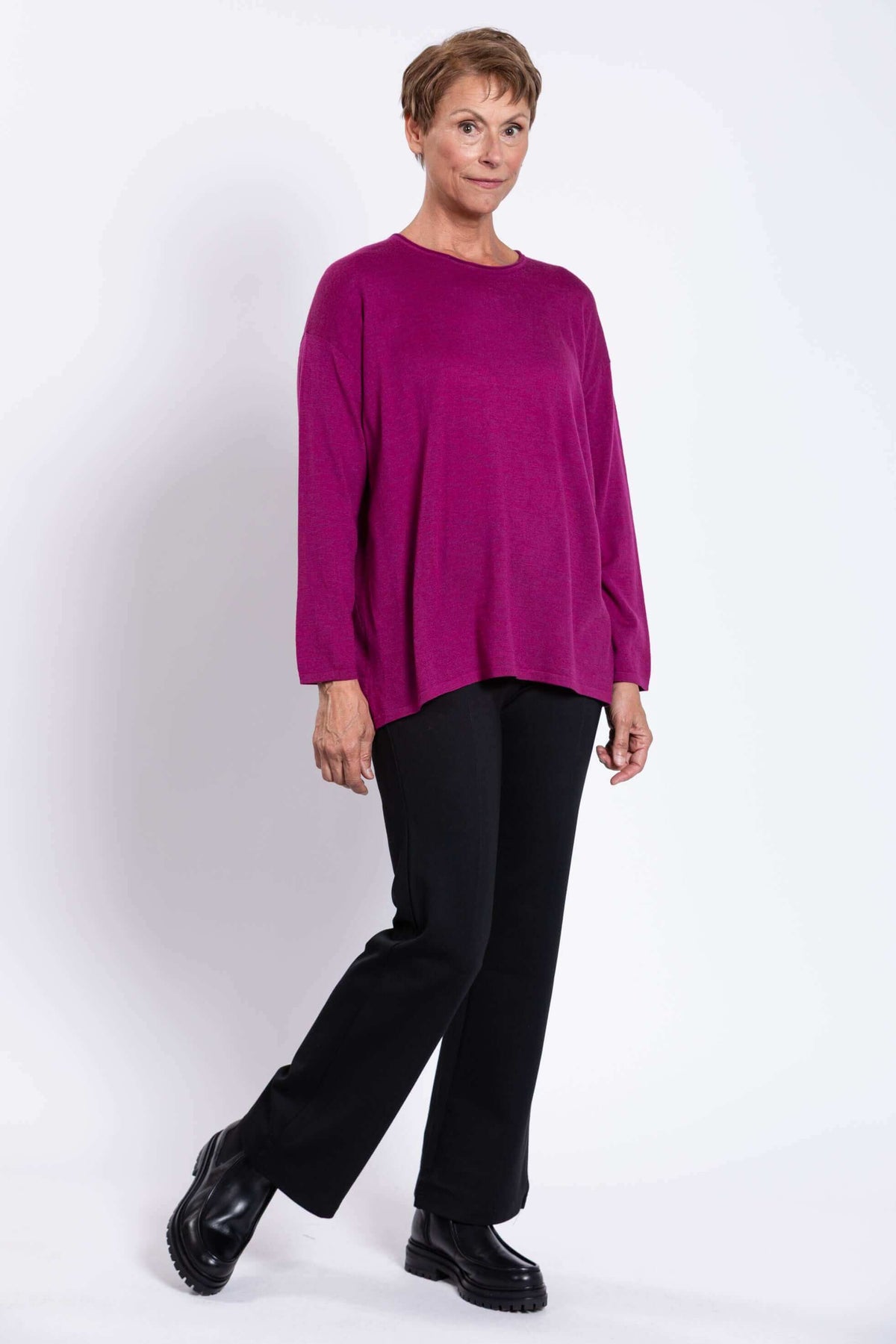 Three-quarter side view of woman in relaxed fit fuchsia sweater and black boots