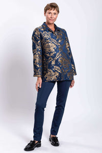 Angled front view of woman in ornate blue and gold jacquard coat and blue pants