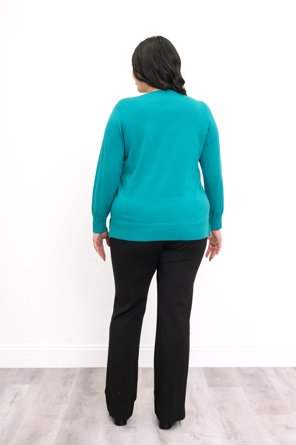 Back view of a woman wearing a hip length turquoise cotton knit sweater highlighting the clean shoulders and hem.