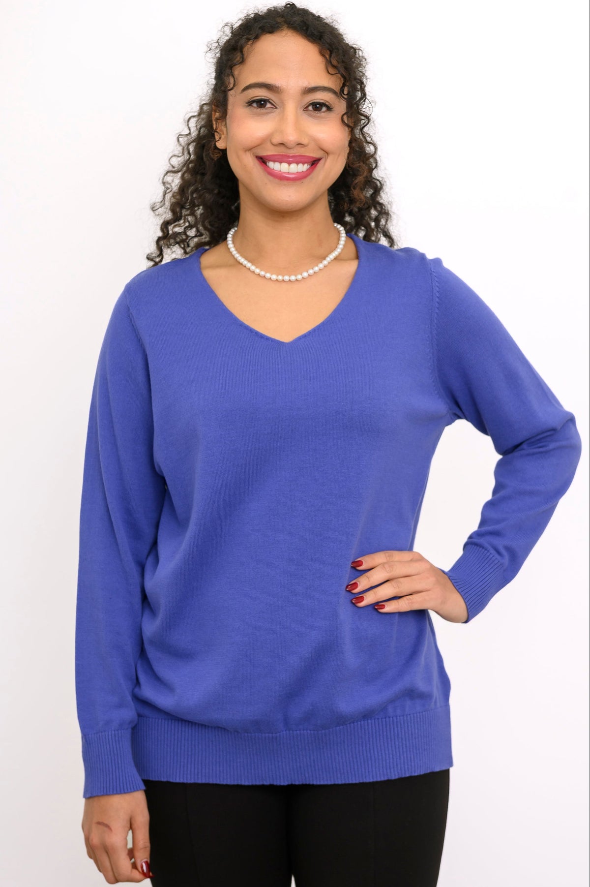 Close up front view of a woman wearing a violet blue v-neck knit sweater paired with black trousers.