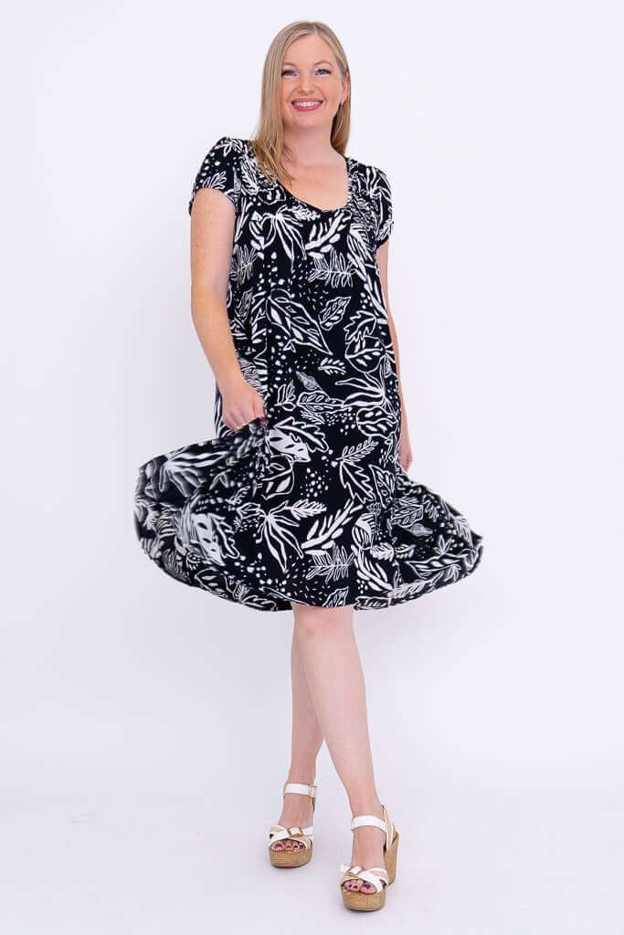 Woman twirling in a black and white flowy dress with leafy pattern