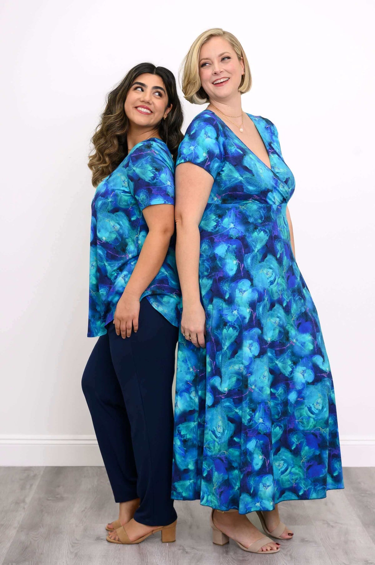 Two women in matching blue floral bamboo outfits, standing back to back and smiling