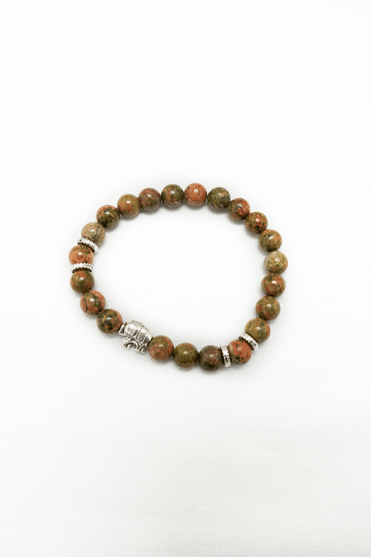 Unakite beaded bracelet with silver accent charms on a white background