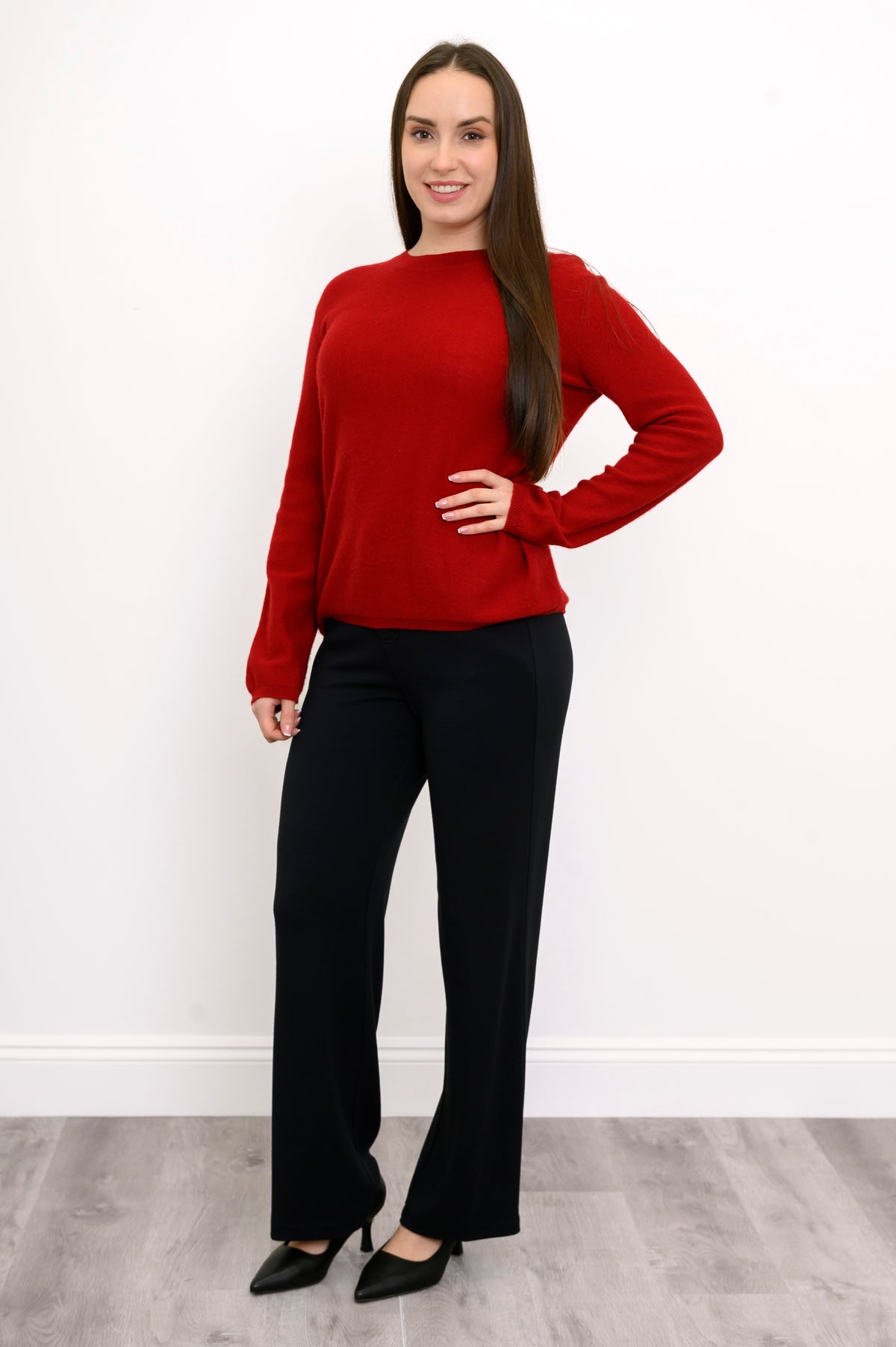 Woman smiling in red knit sweater, relaxed fit black pants, and black pumps