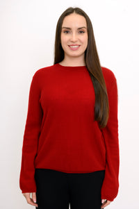 Woman wearing a red long sleeve sweater and black pants on a white background, front view