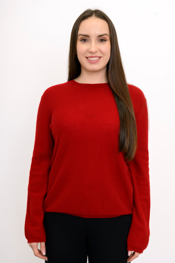 Woman wearing a red long sleeve sweater and black pants on a white background, front view