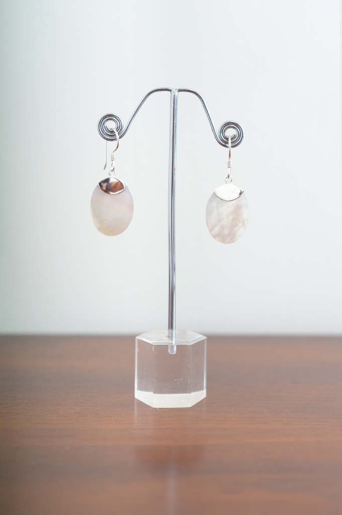 A pair of sterling silver earrings with flat circle pearl pendants displayed on a metal stand, front view
