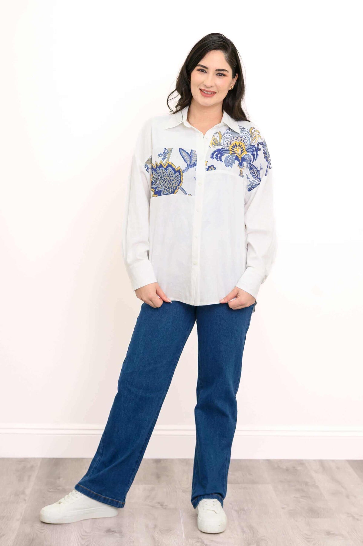 Woman standing in white blouse with blue and gold floral design, hands in pockets