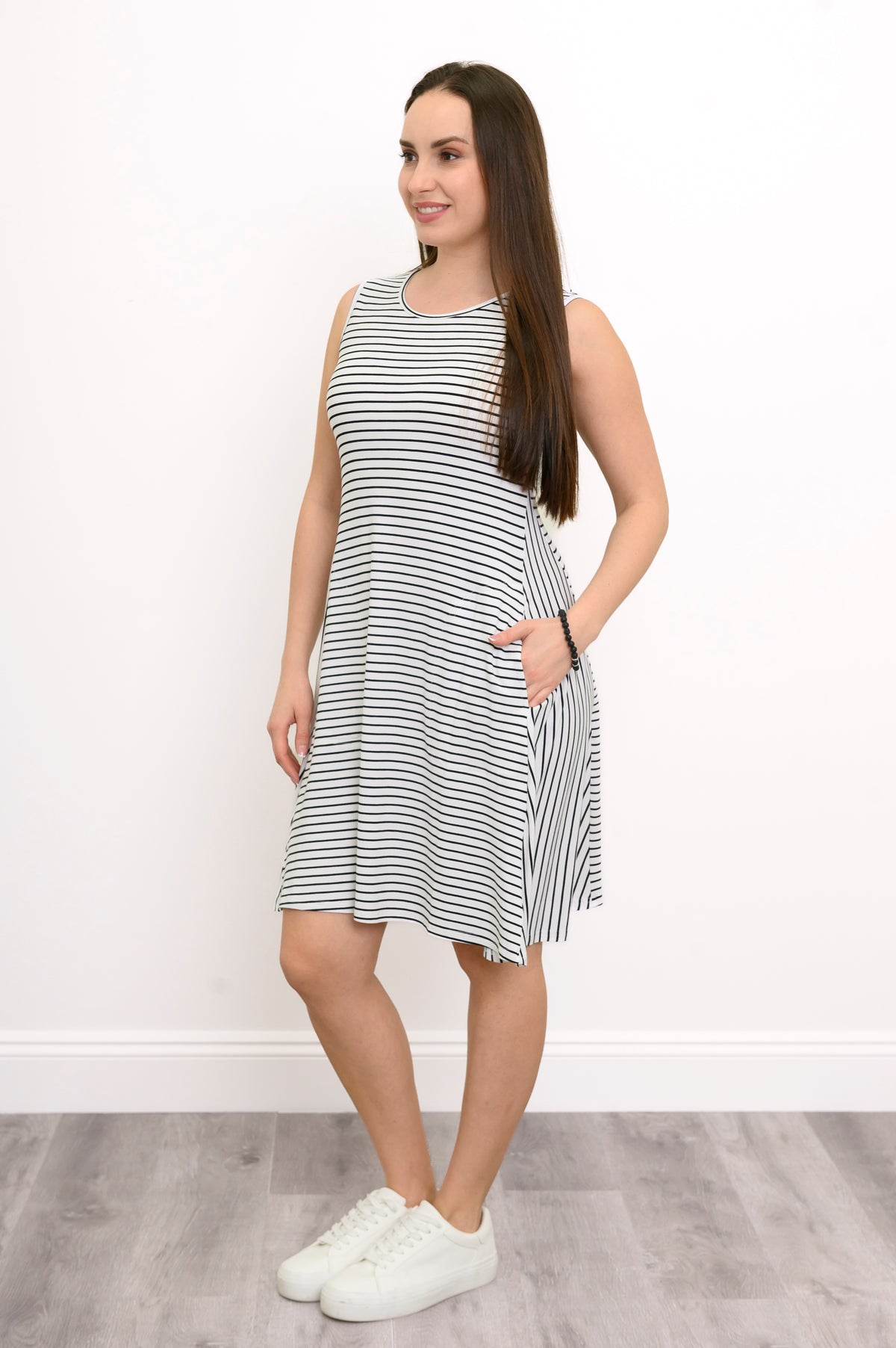 Side view of a woman posing with hands in pockets wearing the Willow Dress in white and black small stripe bamboo fabric.