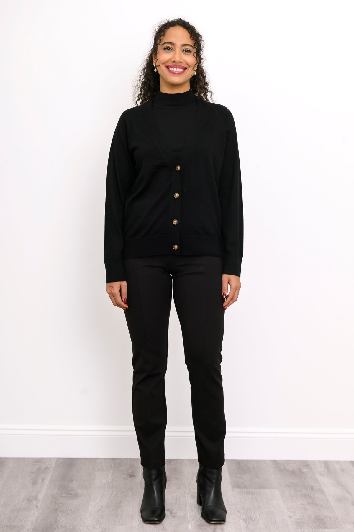 Full length view of a woman wearing a black merino wool v-neck cardigan sweater and black pants.