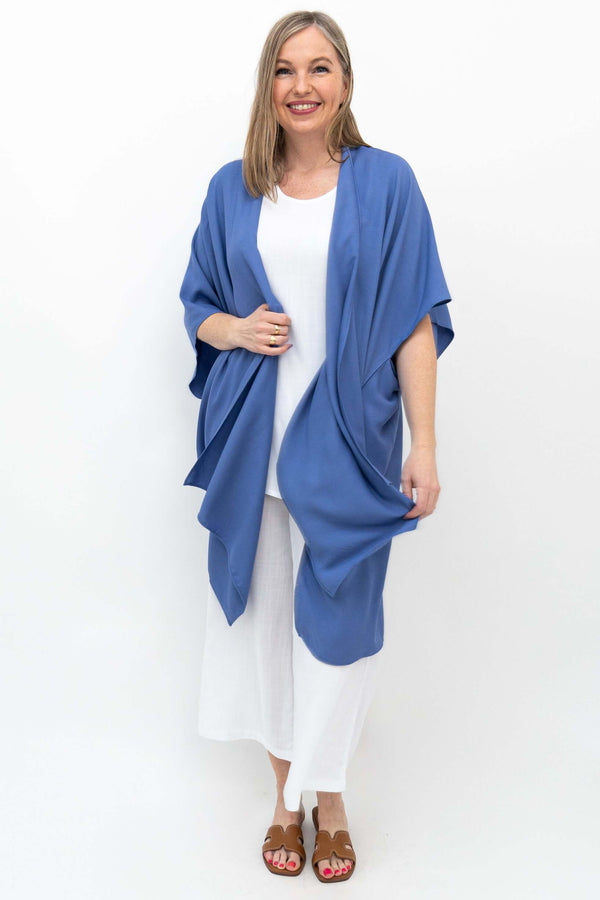 Woman adjusting blue Darcy Kimono Wrap styled with white pants