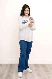 Woman adjusting cuff of white blouse with blue and gold floral accents, standing