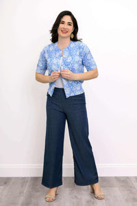 Woman smiling and buttoning a blue floral cropped cardigan