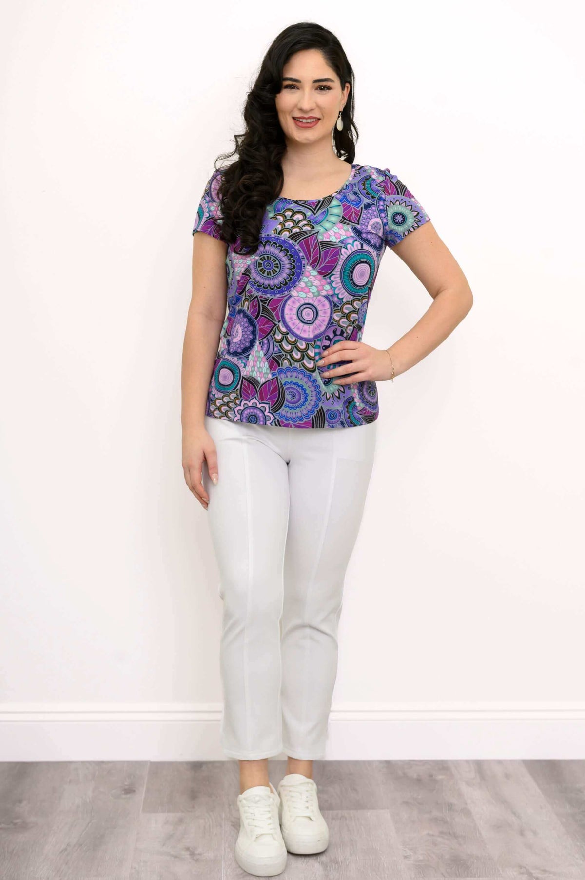 Woman standing, front view, in purple mandala print bamboo top and white pants