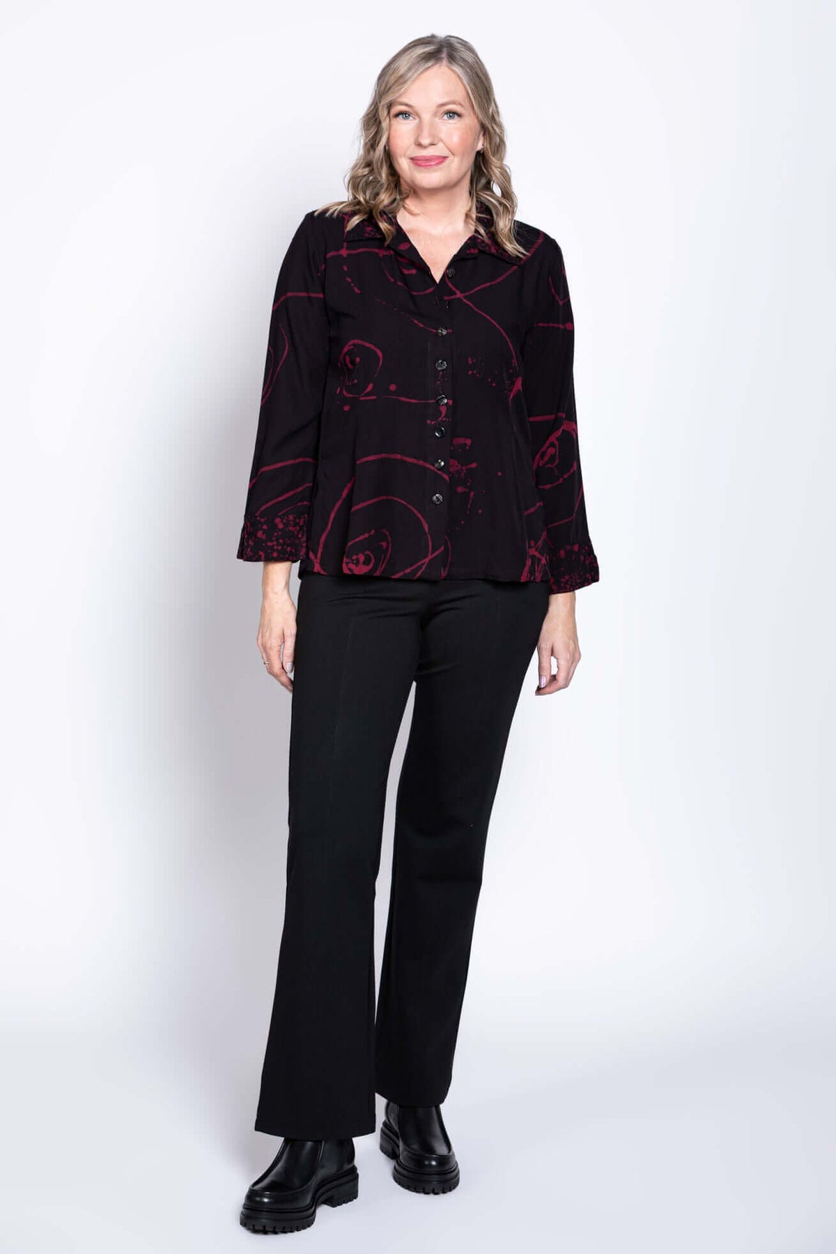 Woman in Ketut blouse and black pants standing against light background