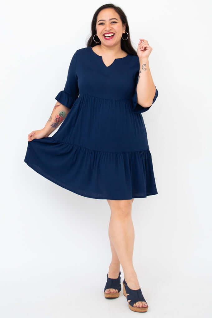 Woman in a navy empire waist dress holding out the skirt and smiling widely