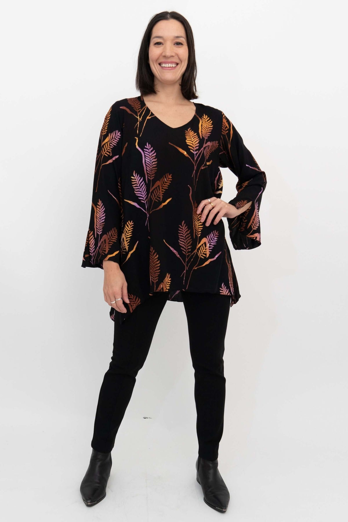 Woman posing with hand on hip, modeling a flowy black top with purple and orange leaf print