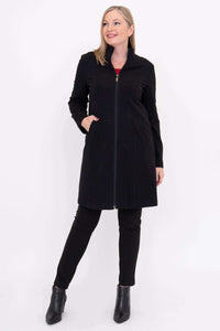 Woman in black coat over black pants and red top, hands in pockets, looking aside