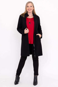 Woman in black coat over red top and black pants, holding lapel open, smiling