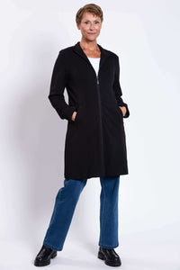 Woman in black cotton coat standing with hands in pockets, wearing blue jeans