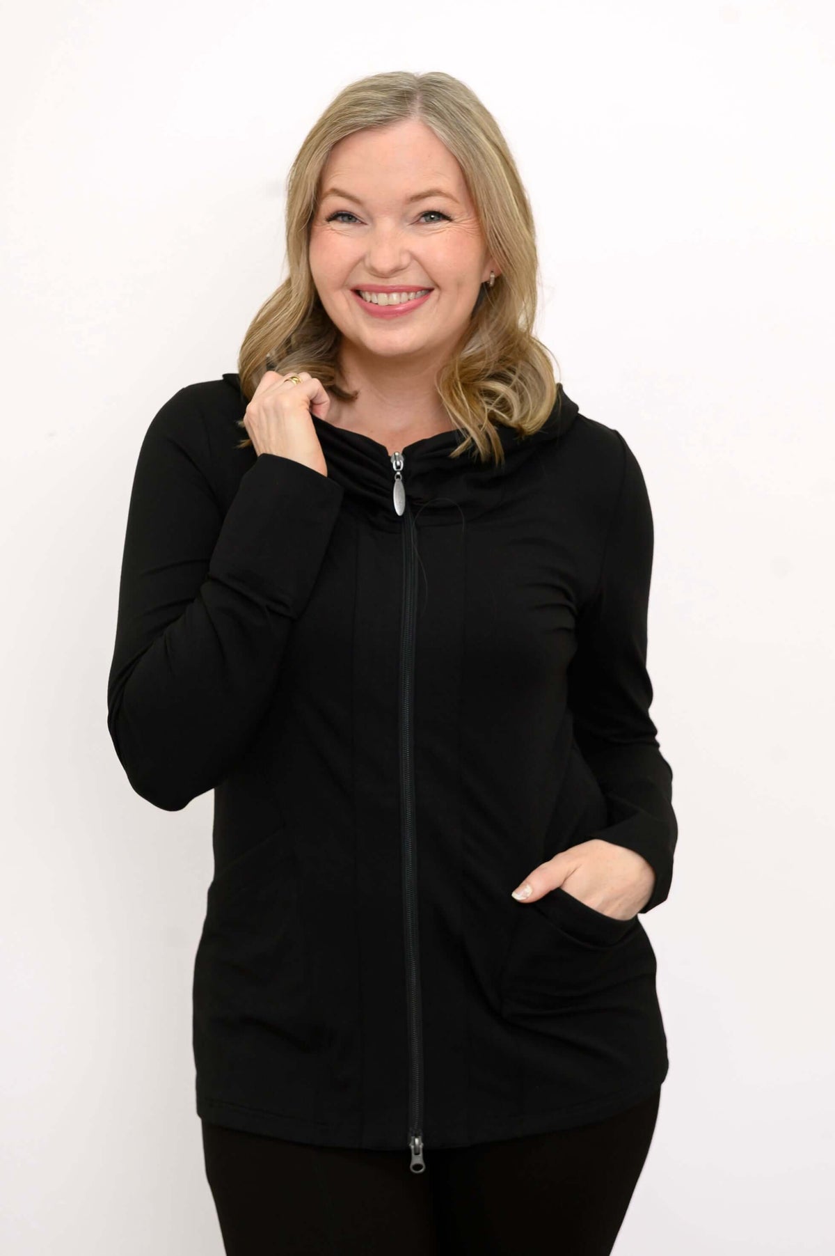 Woman smiling and wearing a black fitted hoodie jacket with pockets