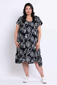 Woman wearing a black flowy dress with white shell print standing facing forward