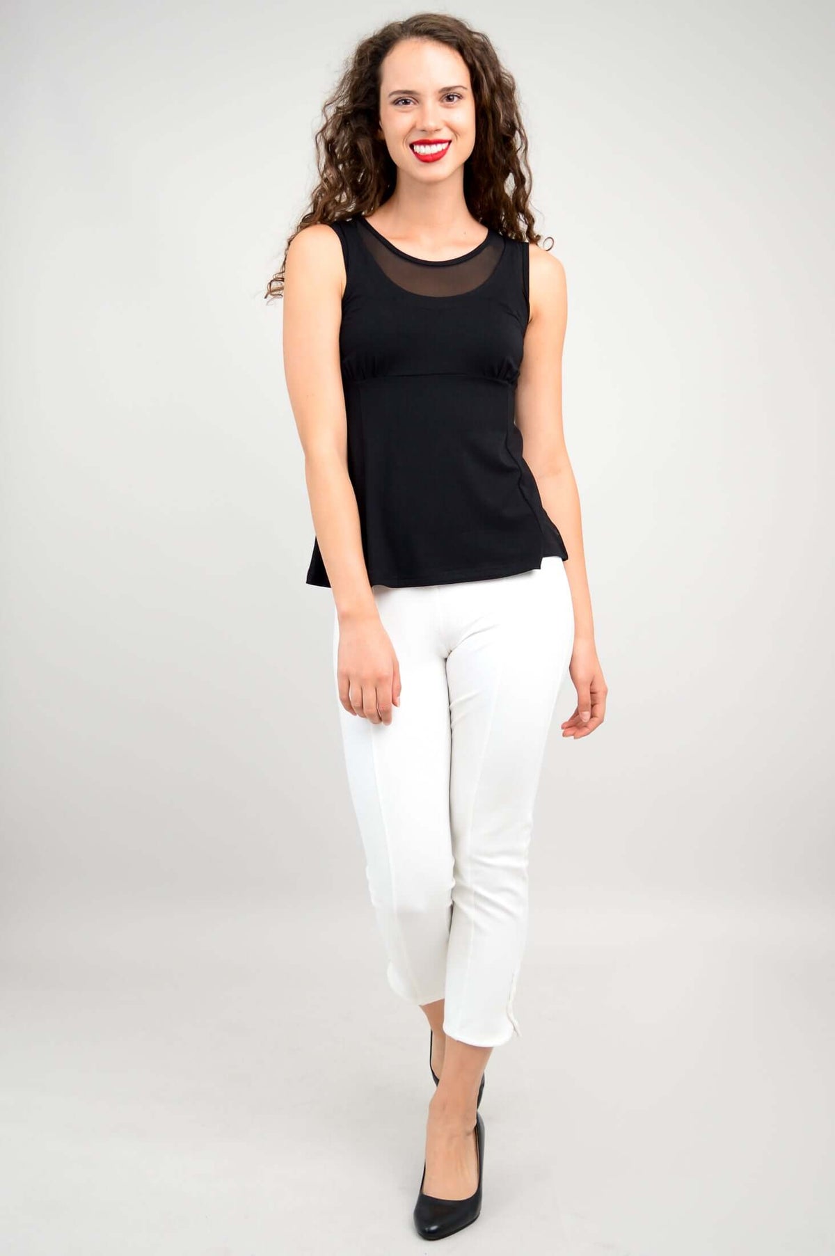 Woman in black tank top with mesh panel, walking forward, wearing white pants