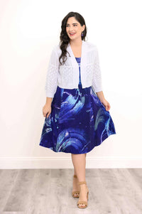 Woman in blue abstract print dress paired with white open-knit cardigan